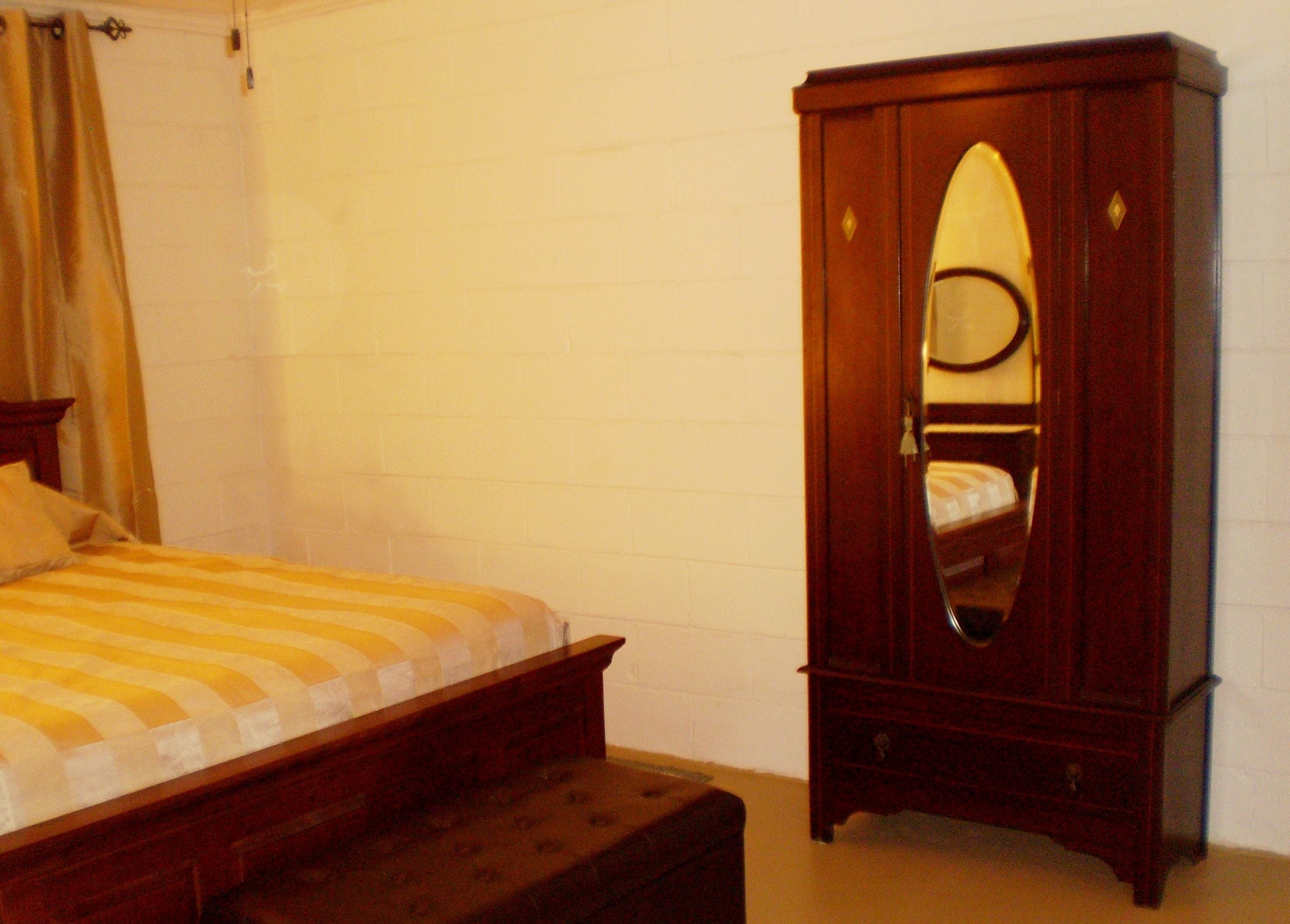 A bedroom with a bed, a wooden wardrobe, and a mirror.