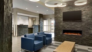 Eine moderne Lobby mit Steinwand, Flachbildfernseher, Kamin, blauem Sitzmöbel und einem Holztisch.
