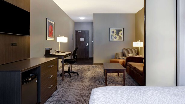 Ein Hotelzimmer mit Bett, Schreibtisch mit Stuhl, einer Couch, einem Fernseher und einer Tür zu einem Flur.