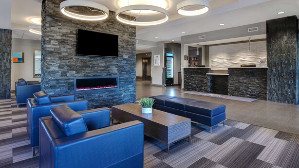 Eine moderne Lobby mit Steinwänden, einem Flachbildfernseher, einem Kamin und blauen Ledersitzmöglichkeiten.