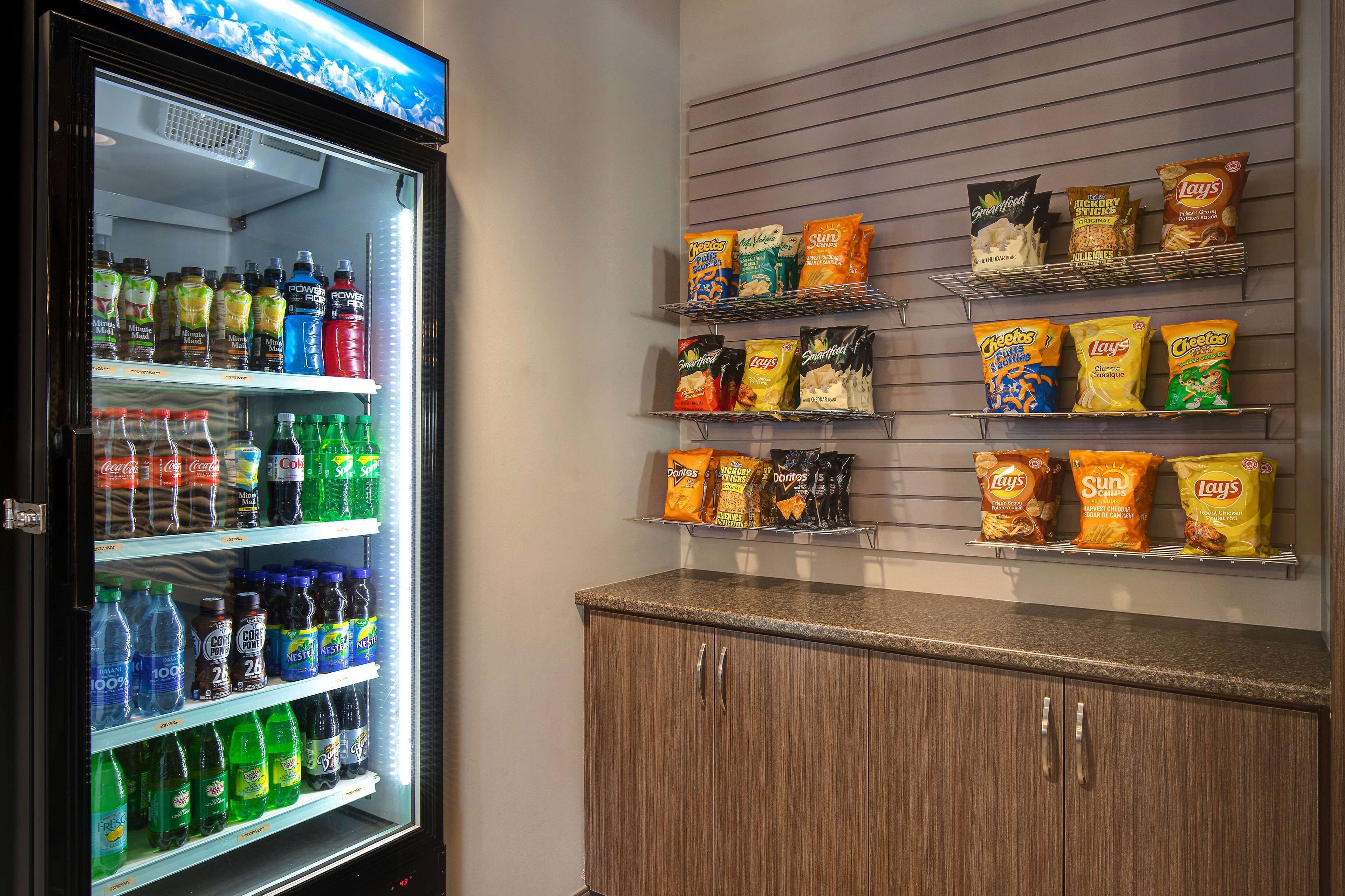Un refrigerador lleno de bebidas, como refrescos, y un estante con aperitivos como papas fritas y galletas.