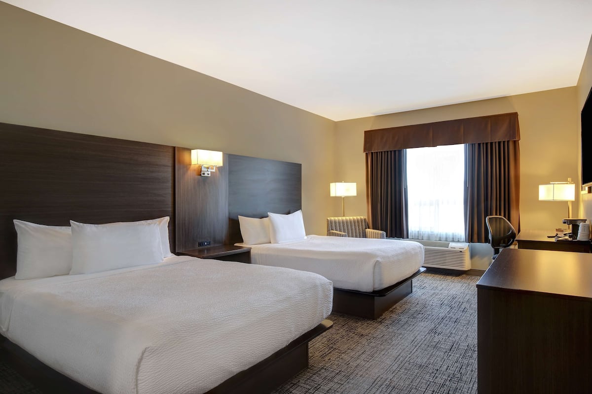 A hotel room with two beds, a desk, a chair, and a large window with curtains.