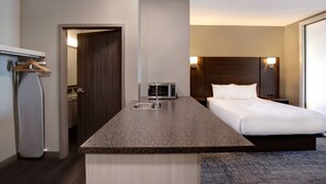Ein Hotelzimmer mit Küchenzeile, einem Bett, einem Nachttisch und einer Wandlampe.