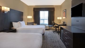 A hotel room with two beds, a desk, a chair, a TV, and a large window with curtains.