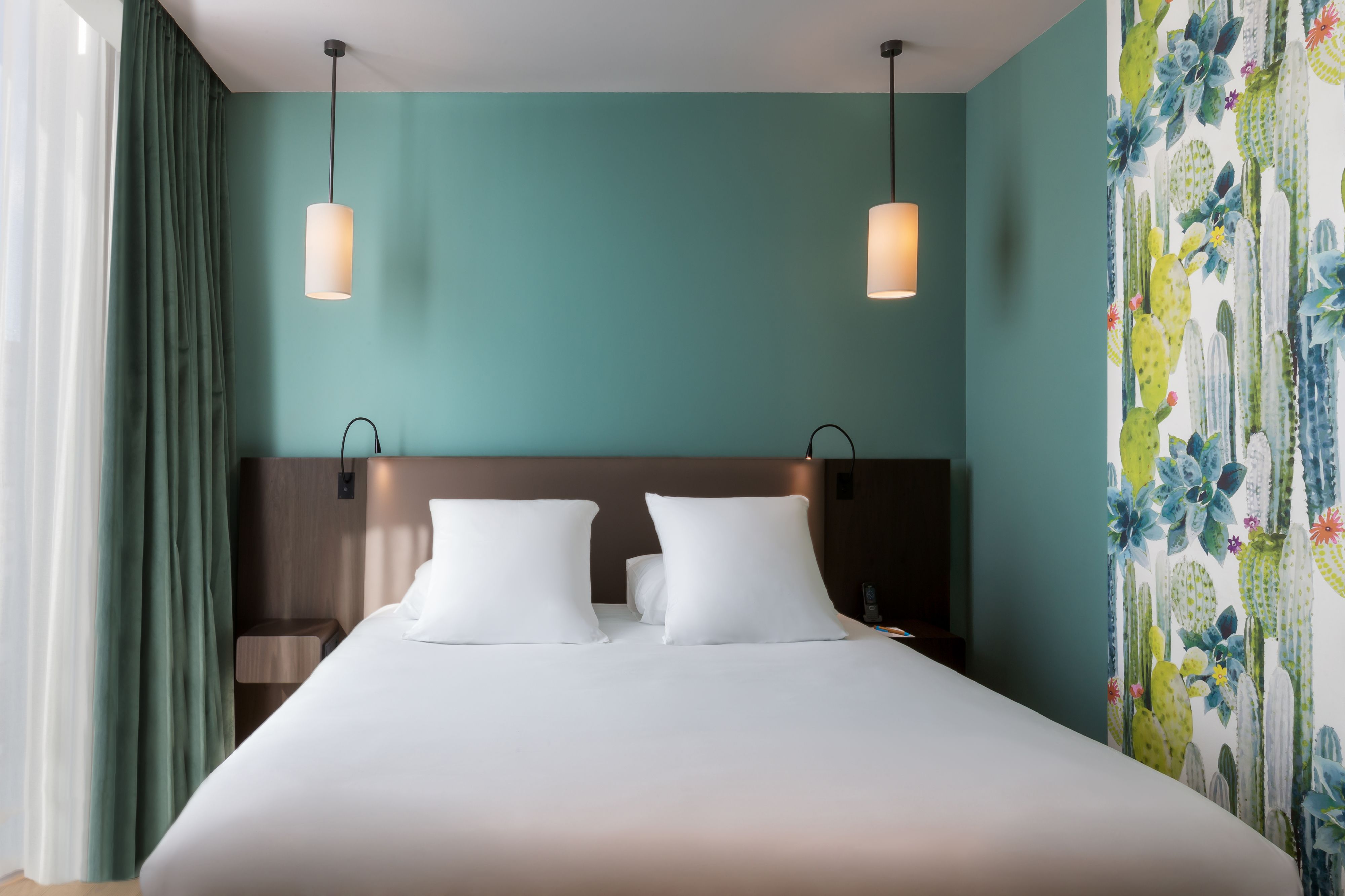 Hotelkamer met een groot bed, twee bedlampen, een hoofdeinde en een muur met een cactustapijt en bloemenmotief.