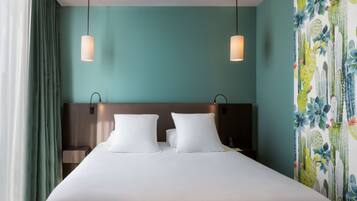 Hotelkamer met een groot bed, twee bedlampen, een hoofdeinde en een muur met een cactustapijt en bloemenmotief.