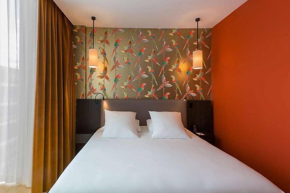 Ein Hotelzimmer mit einem großen Bett, zwei Nachttischlampen, einem Kopfteil und einer Wand mit Vogelmotiv.