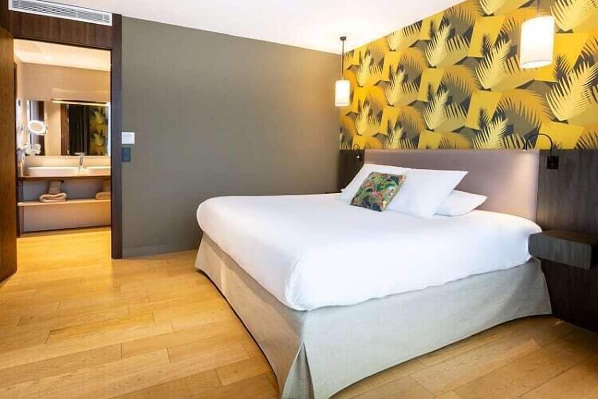 Ein Hotelzimmer mit Bett, Holzboden, Badezimmer mit Spiegel und Wand mit Muster.