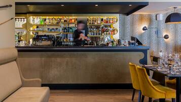 A bar area with a bartender, a variety of liquor bottles, and a seating area with yellow chairs.