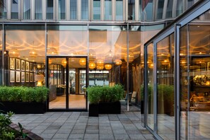 A modern hotel entrance with glass doors, indoor plants, and hanging lights. - Hotel l'Arbre Voyageur (Lille)