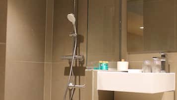 Une salle de bain moderne avec une douche à parois de verre, un lavabo blanc avec un miroir et des serviettes soigneusement pliées sur une étagère.