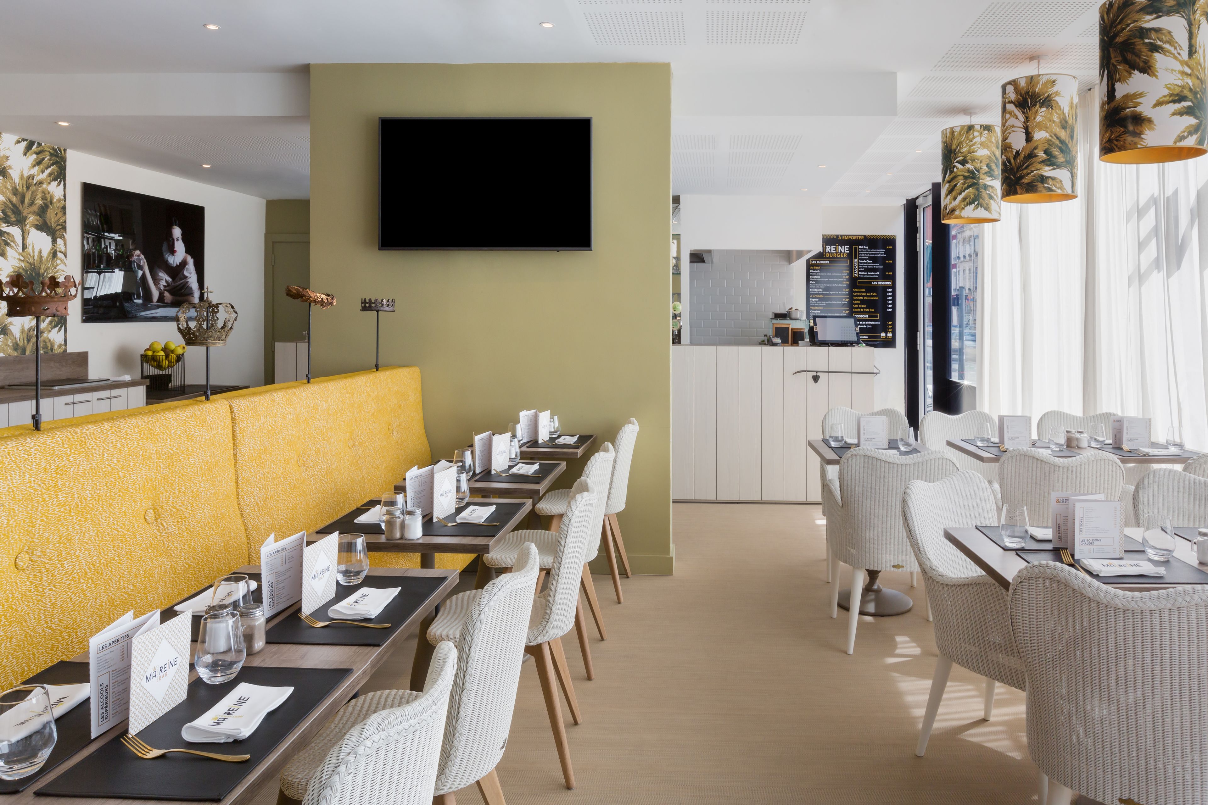 A modern restaurant with a long dining table, white wicker chairs, and a yellow partition.