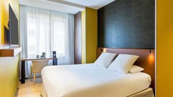 A hotel room with a large bed, a desk, a chair, and a TV mounted on the wall.