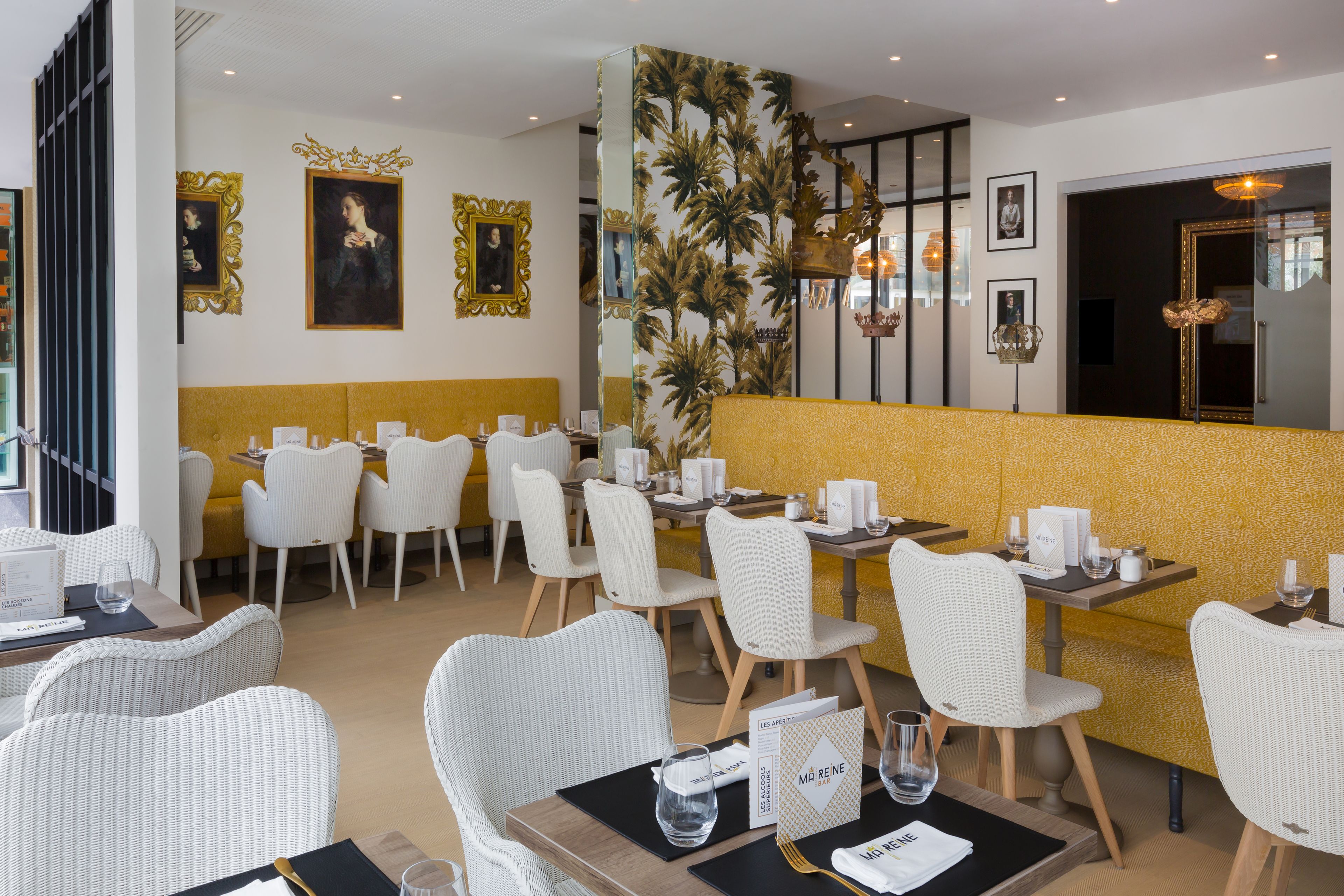 A restaurant with white wicker chairs, yellow cushioned booths, and framed artwork on the walls.