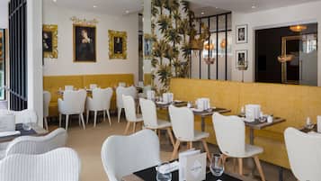 A restaurant with white wicker chairs, yellow cushioned booths, and framed artwork on the walls.