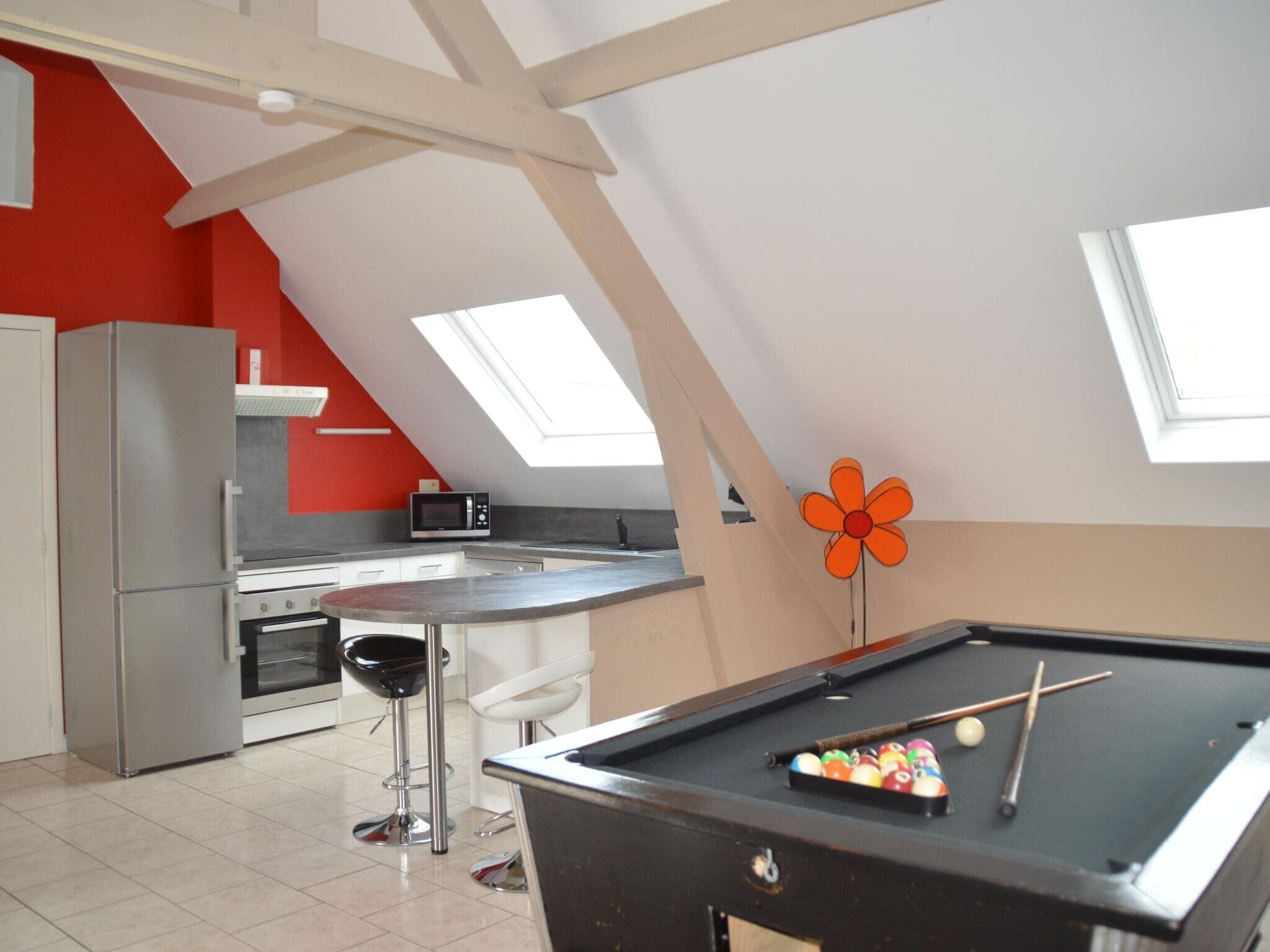 A kitchen with a pool table, a microwave, and a refrigerator.