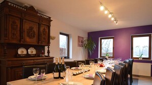A dining area with a long table set for a meal, wooden cabinets, and large windows. - Holiday Home in Waimes with Pool & Sauna (Waimes)