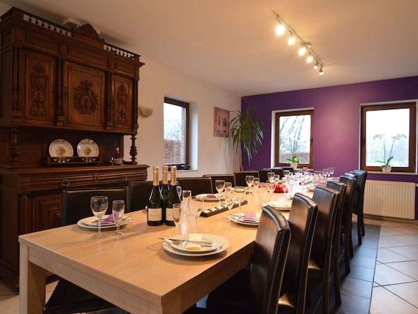 Un espace repas avec une longue table dressée pour le repas, des meubles de rangement en bois et de grandes fenêtres.