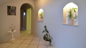 A hallway with white walls, tiled floor, and two potted plants on shelves. - Holiday Home in Waimes with Pool & Sauna (Waimes)