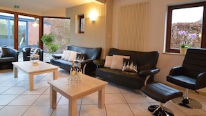 A modern lounge area with leather sofas, a wooden coffee table, and a bar stool. - Holiday Home in Waimes with Pool & Sauna (Waimes)