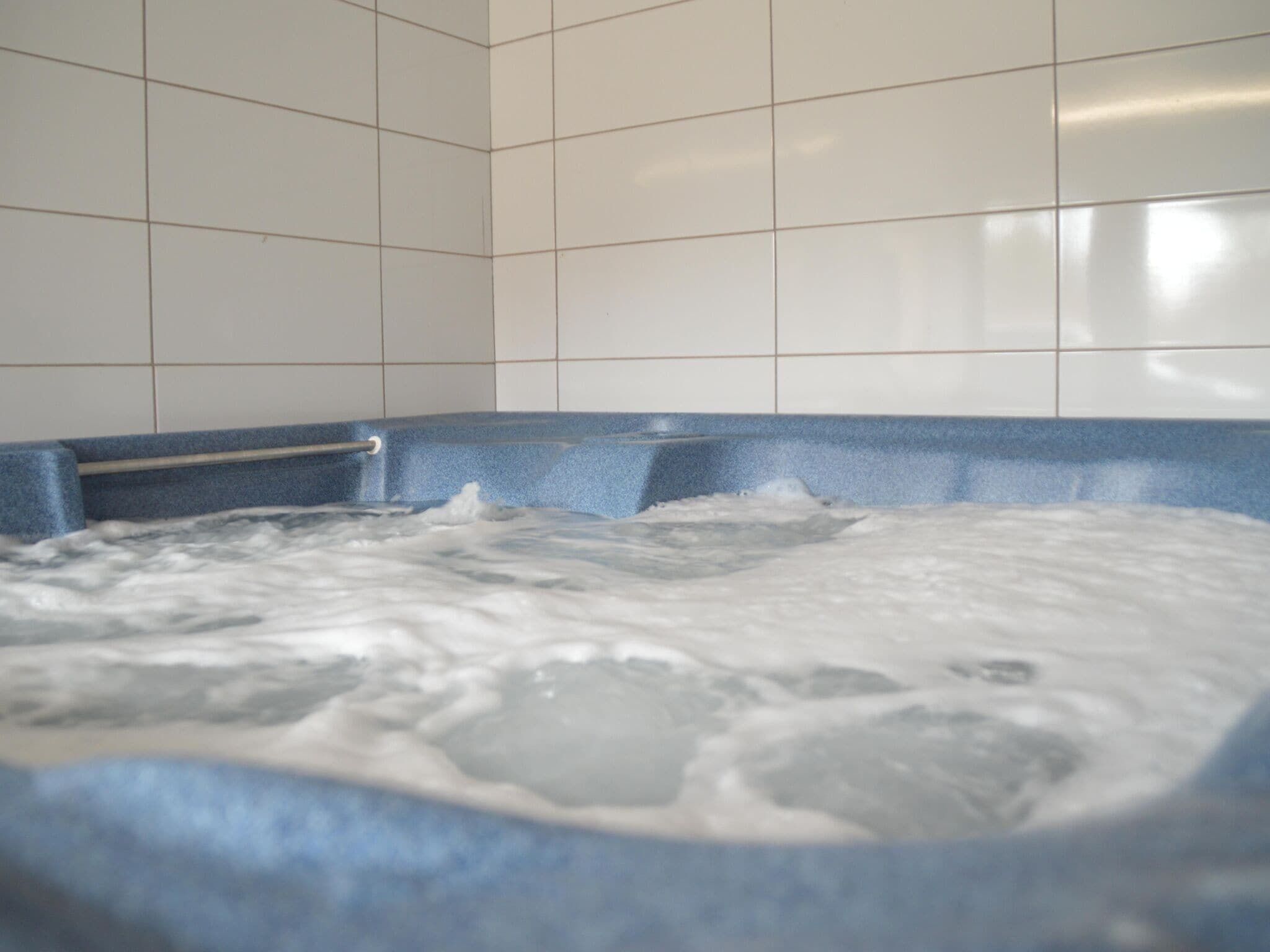 A hot tub with a blue edge and a metal railing, surrounded by white tiled walls.