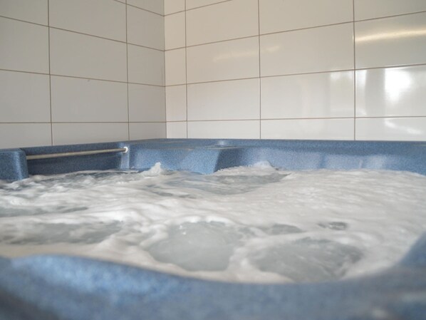 A hot tub with a blue edge and a metal railing, surrounded by white tiled walls.