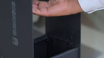 A hand reaching into a sanitizer dispenser with the instruction 'SANITIZE HERE' on the front.