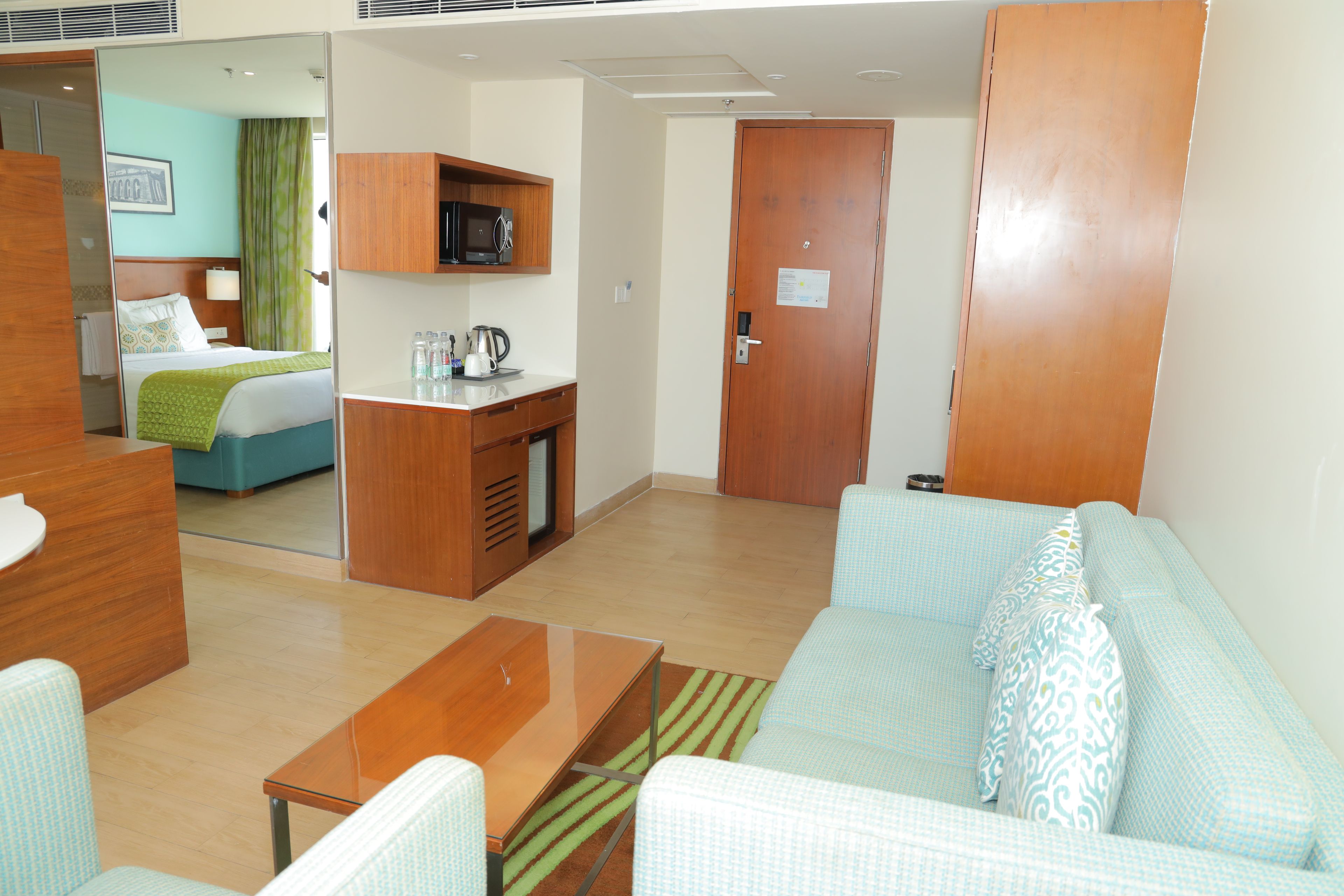 A hotel room with a bed, a desk, a kitchenette, a sofa, and a door.