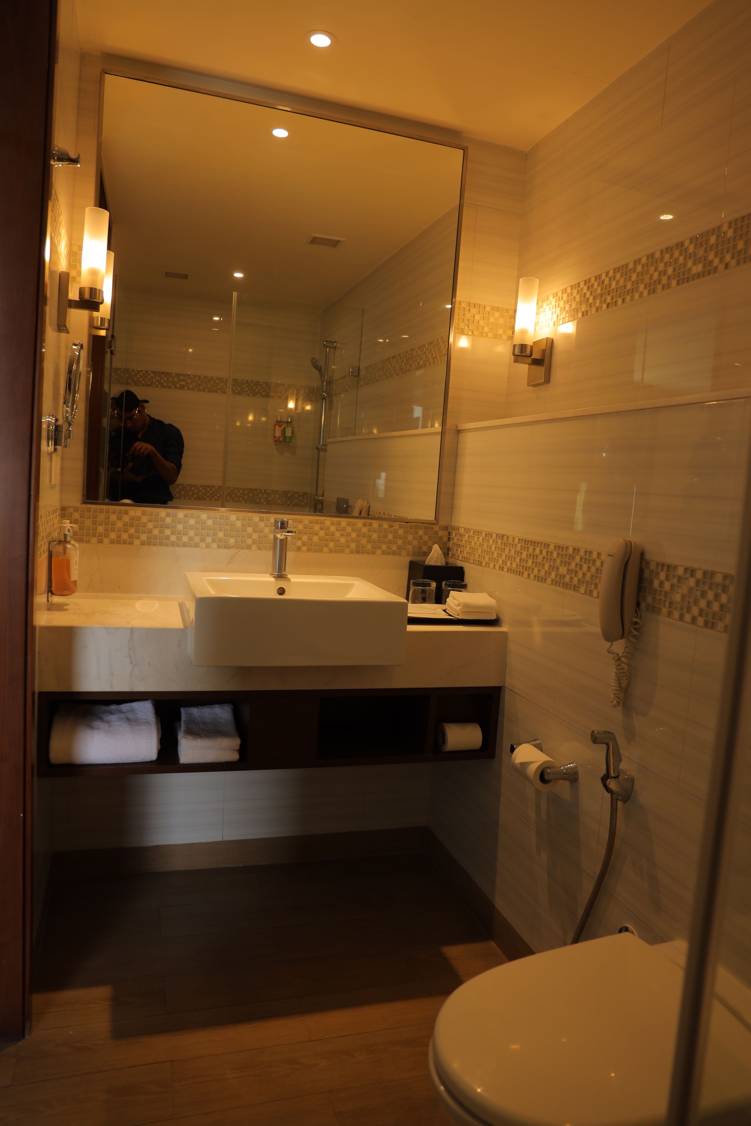 Een badkamer met een grote spiegel, twee wastafels, een toilet en een douche.