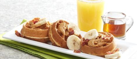 A breakfast plate with pancakes, bananas, and bacon, accompanied by a glass of orange juice and a pitcher of honey.