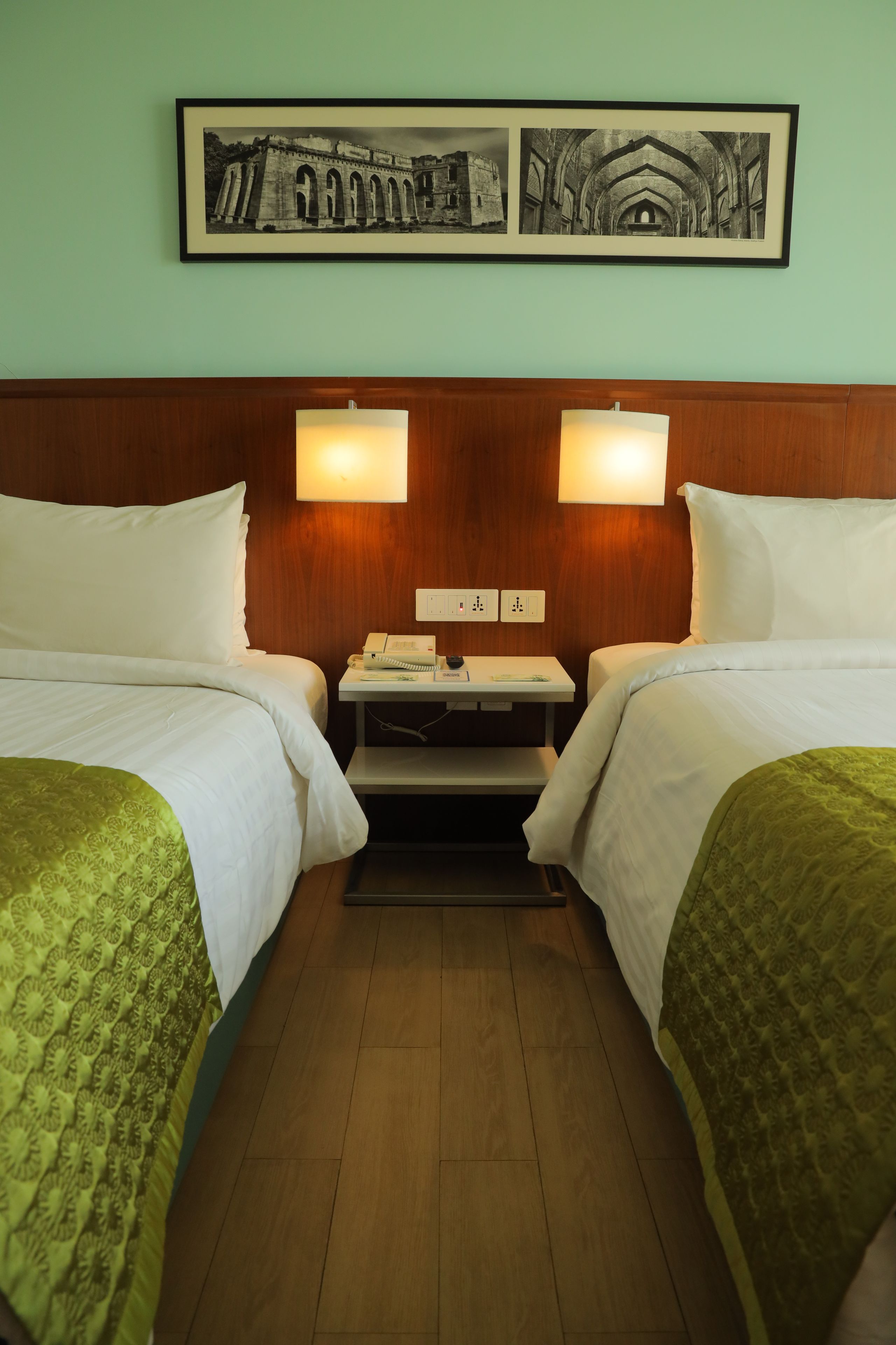 Habitació d'hotel amb dos llits, una tauleta de nit, una làmpada i un quadre a la paret.