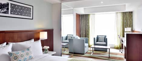 Une chambre d’hôtel avec un grand lit, un bureau, une chaise et un canapé. Il y a une fenêtre avec des rideaux et une vue sur l’extérieur.