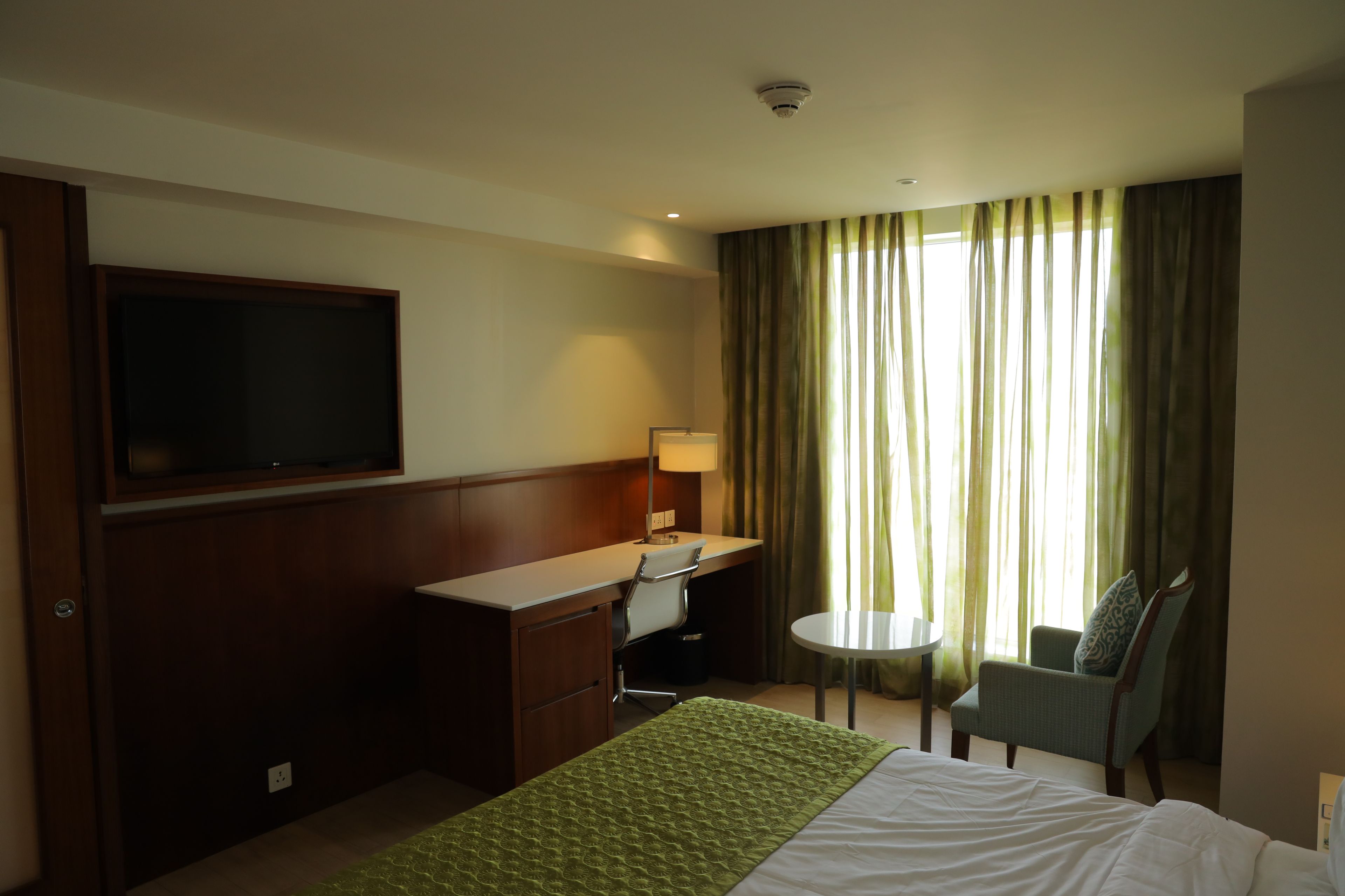 A hotel room with a bed, a desk, a chair, a television, and a window with curtains.