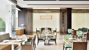 Un comedor moderno con varias mesas y sillas, un separador de vidrio y vistas a zonas verdes exteriores.
