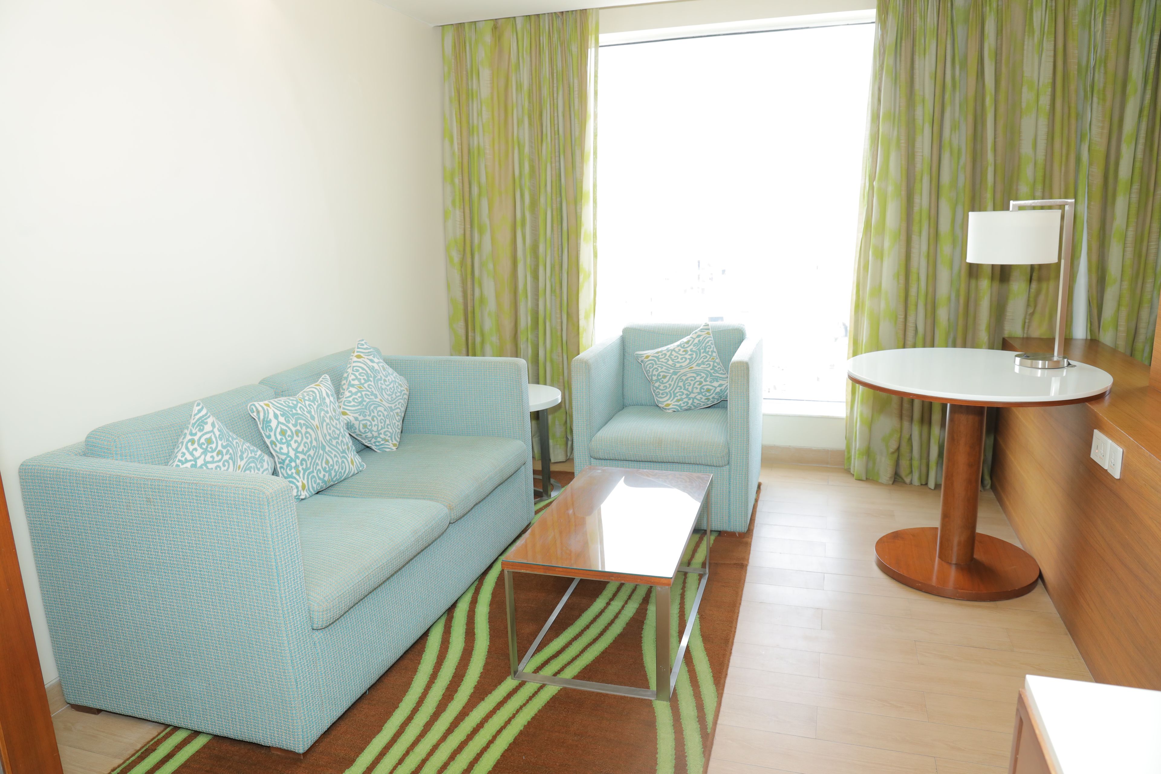 A room with a sofa, a chair, a small table, a lamp, and a window with curtains.
