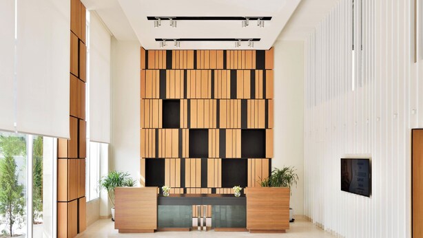 Un área de recepción moderna con un panel de madera, mostrador de recepción y plantas en macetas.