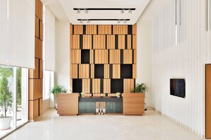 Un área de recepción moderna con un panel de madera, mostrador de recepción y plantas en macetas.