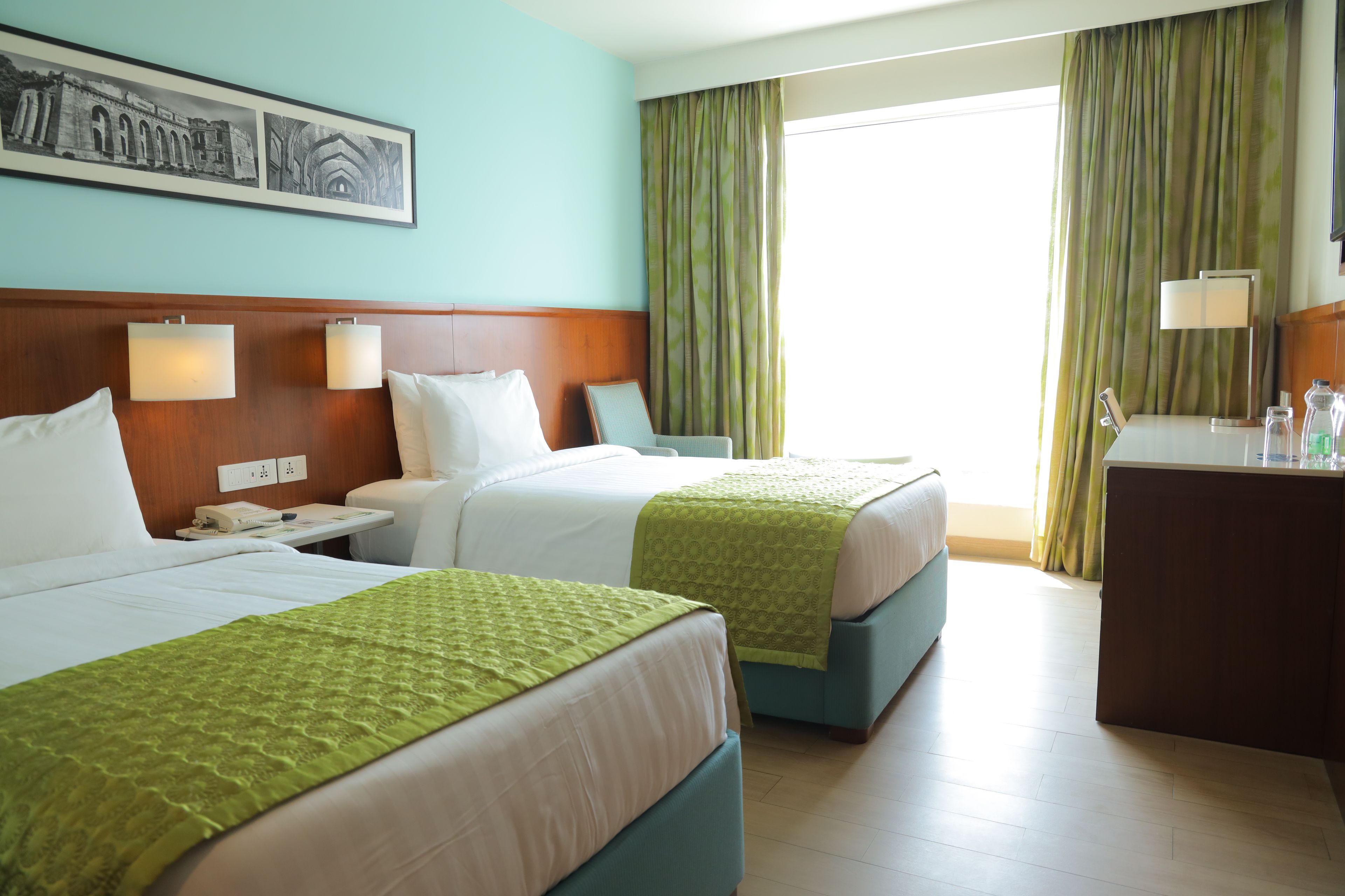 A hotel room with two beds, a desk, a telephone, and a painting on the wall.