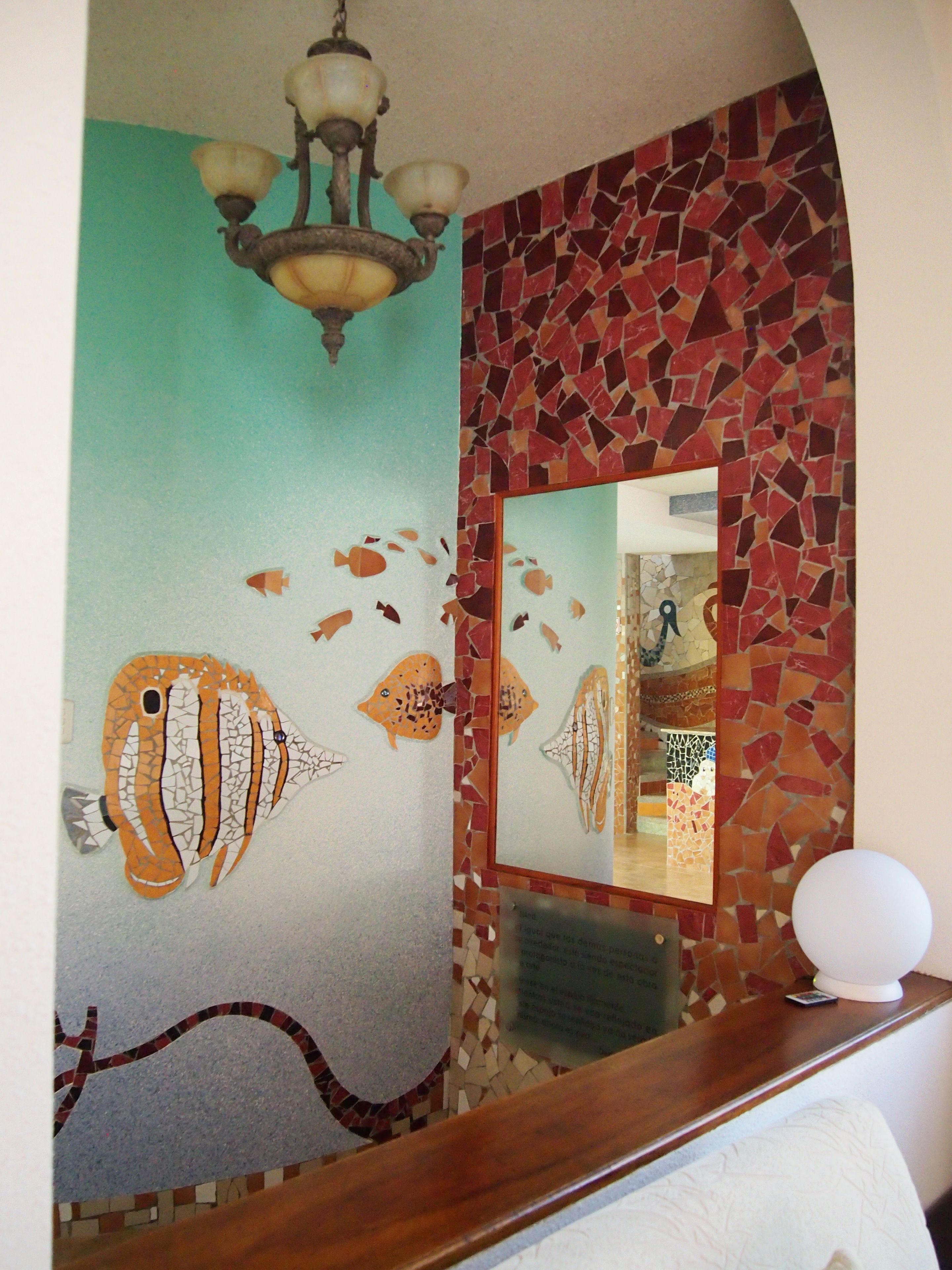 Une salle de bain décorée avec une mosaïque représentant des poissons sur un mur, un miroir et un lustre.