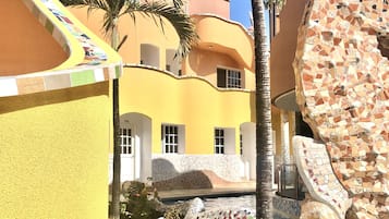 A courtyard with a mosaic-tiled bench, palm trees, and a building with a yellow facade.