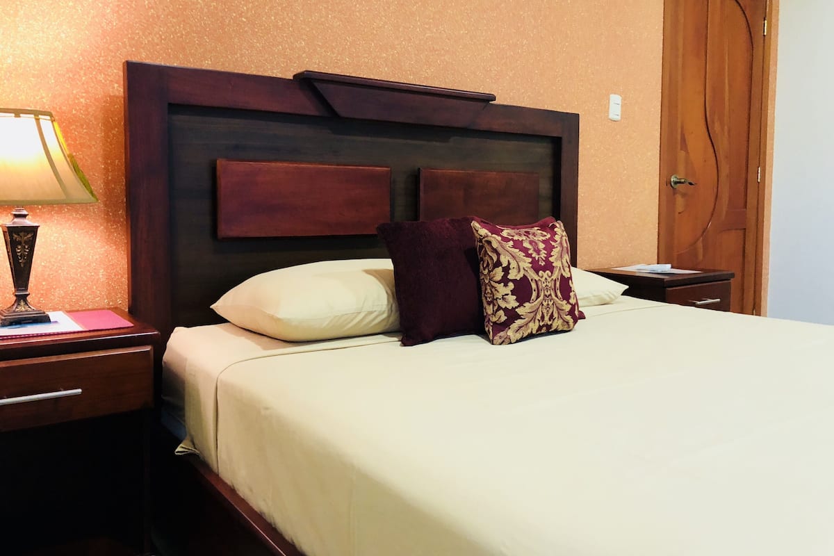 Une chambre d’hôtel avec un lit, une table de chevet, une lampe et une porte en bois.