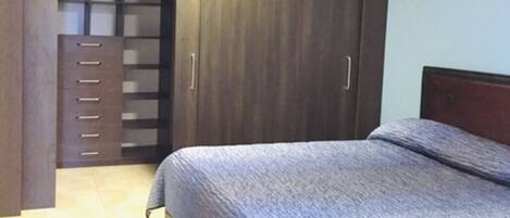 A bedroom with a bed, a wardrobe, and a small cabinet.