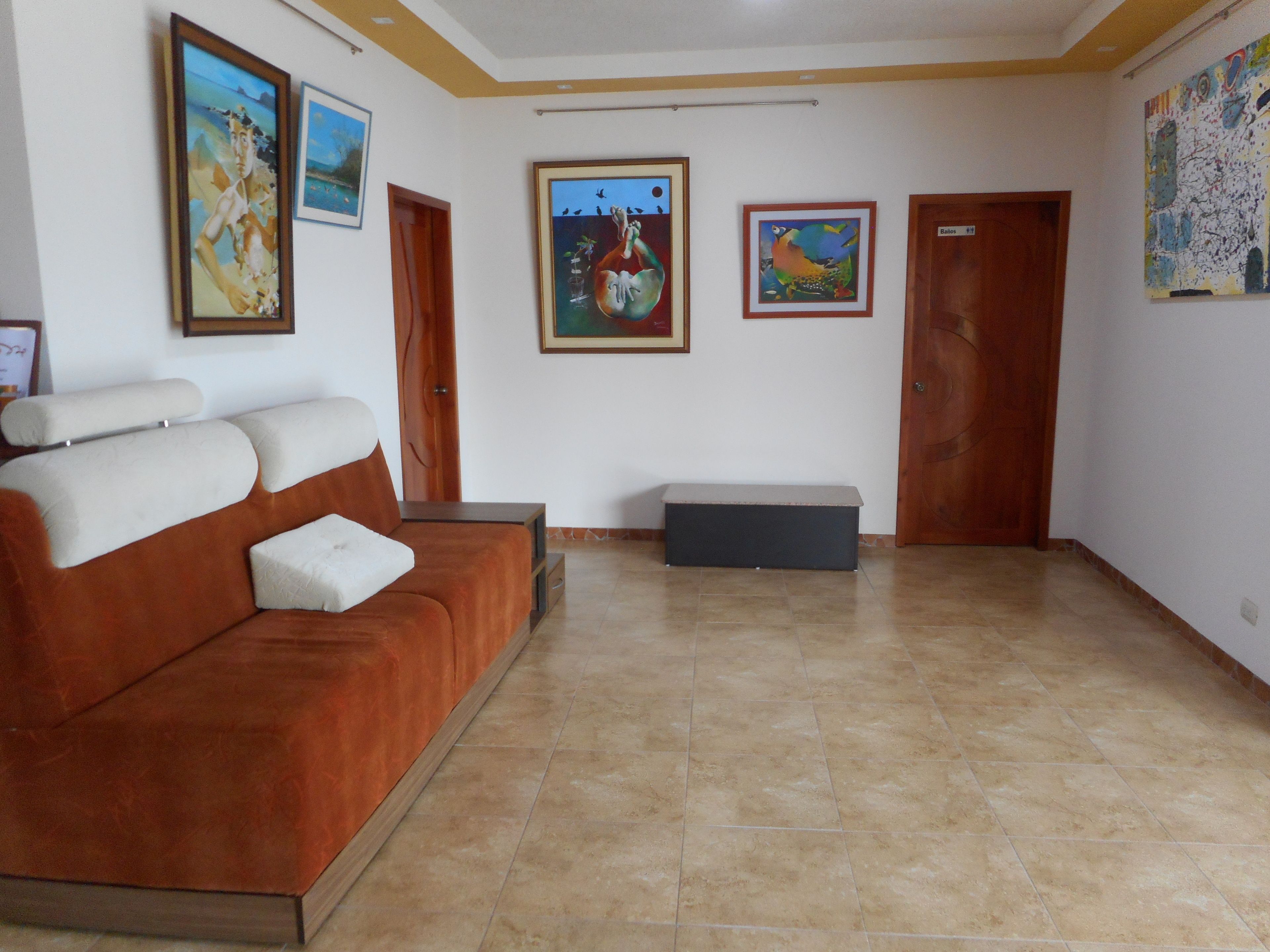 A room with a brown sofa, a bench, and a tiled floor. There are three doors and four framed artworks on the walls.