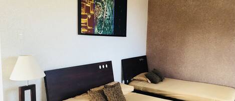 Habitación de hotel con dos camas, una mesita de noche con lámpara, un cuadro en la pared y un equipo de aire acondicionado.
