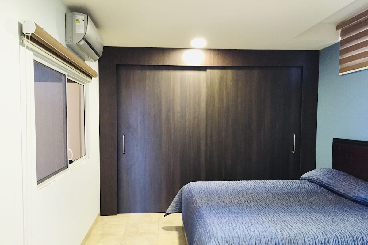 Une chambre à coucher comprenant un lit, une armoire, une fenêtre avec des stores et un appareil de climatisation.