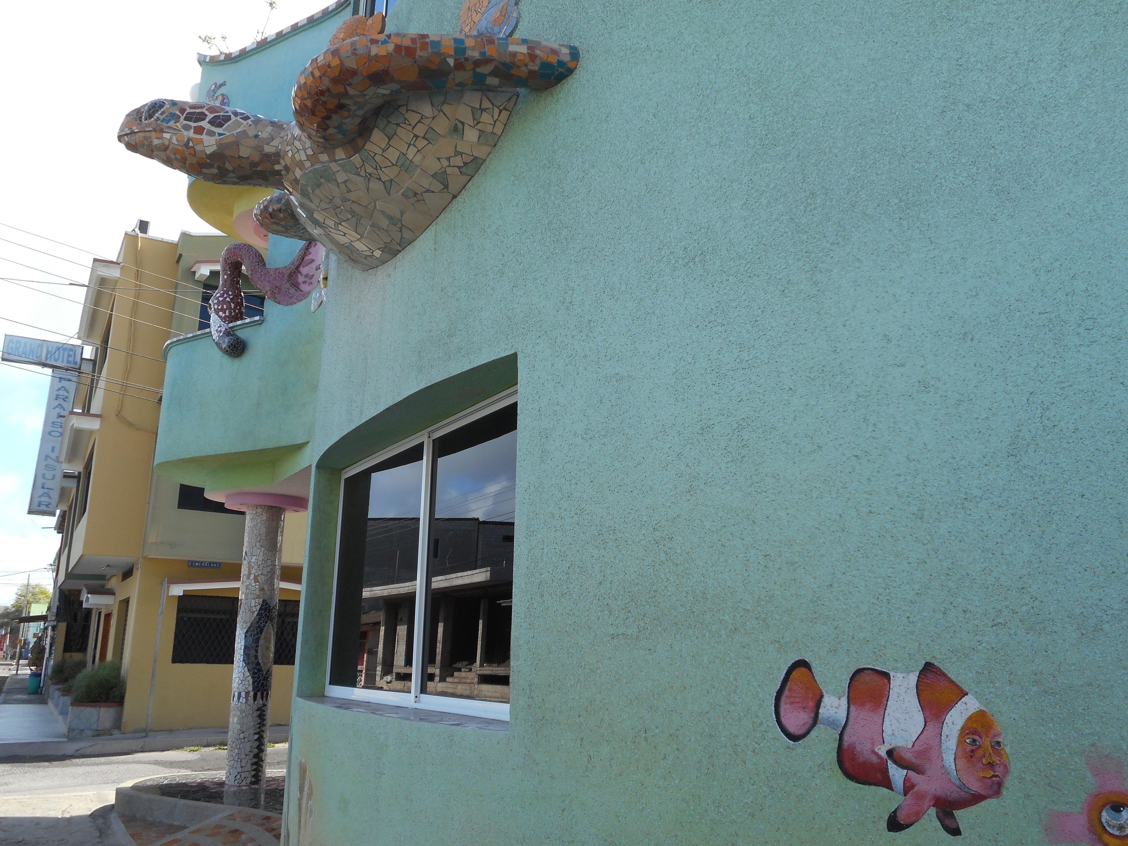A building with a mosaic snake design on the facade, a window, and a painted clownfish.