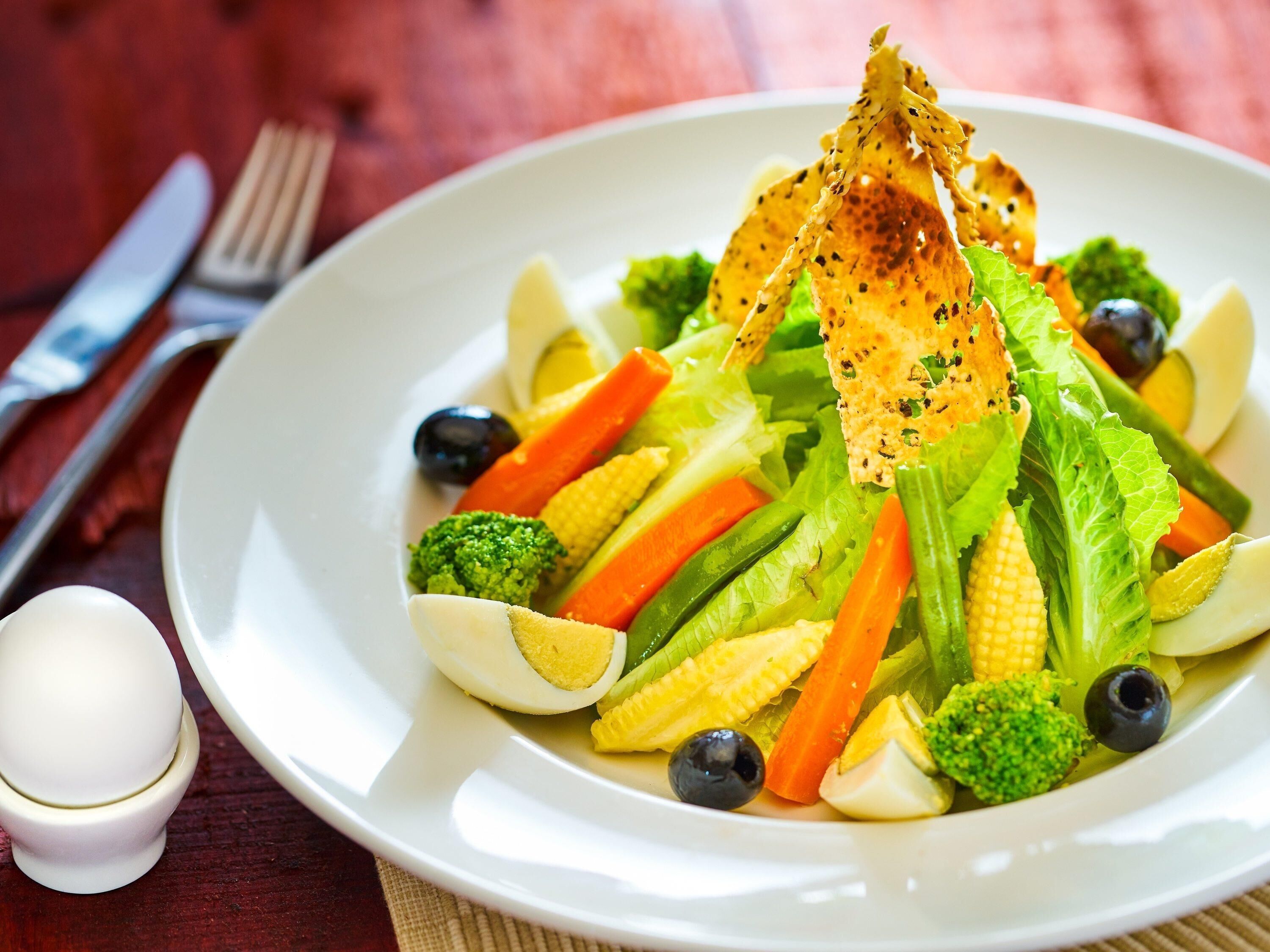 A plate of mixed vegetables including broccoli, carrots, and corn, with a piece of bread on top.