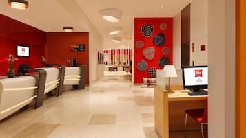Zona de recepción de un hotel con pared roja, mostrador de recepción y un monitor de computadora que muestra el nombre del hotel.