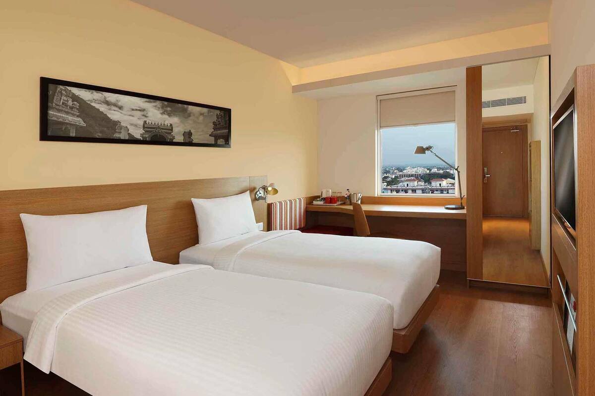 Habitación de hotel con dos camas, un escritorio, una silla, un televisor y una ventana con vistas.