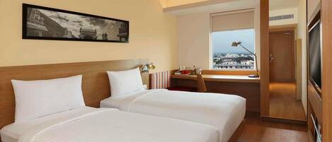 A hotel room with two beds, a desk, a chair, a TV, and a window with a view.